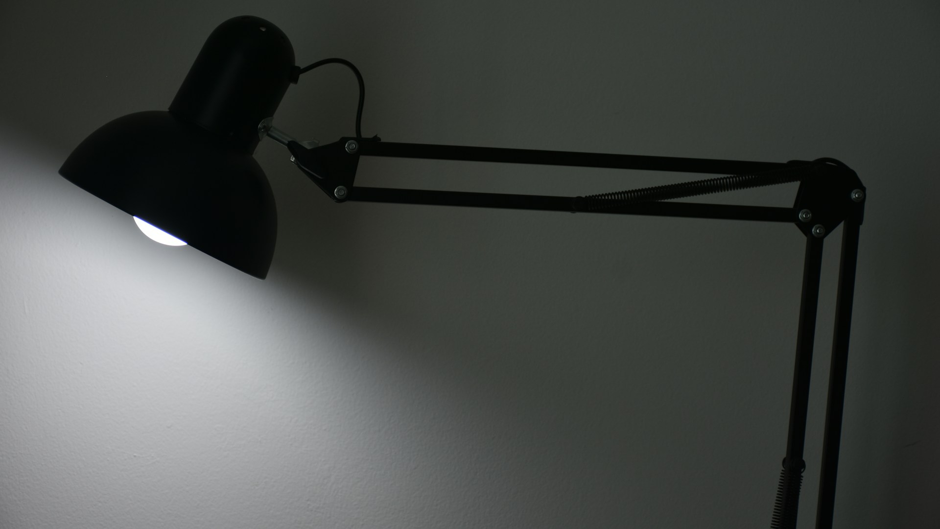 A black adjustable desk lamp illuminates a wall.