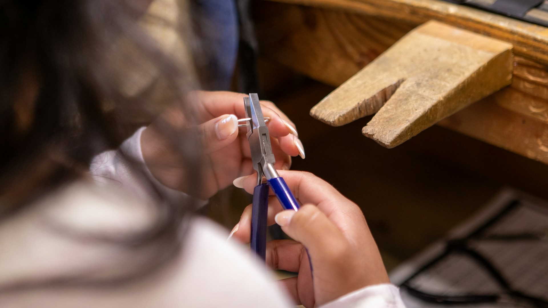 A person works on jewelry with pliers.